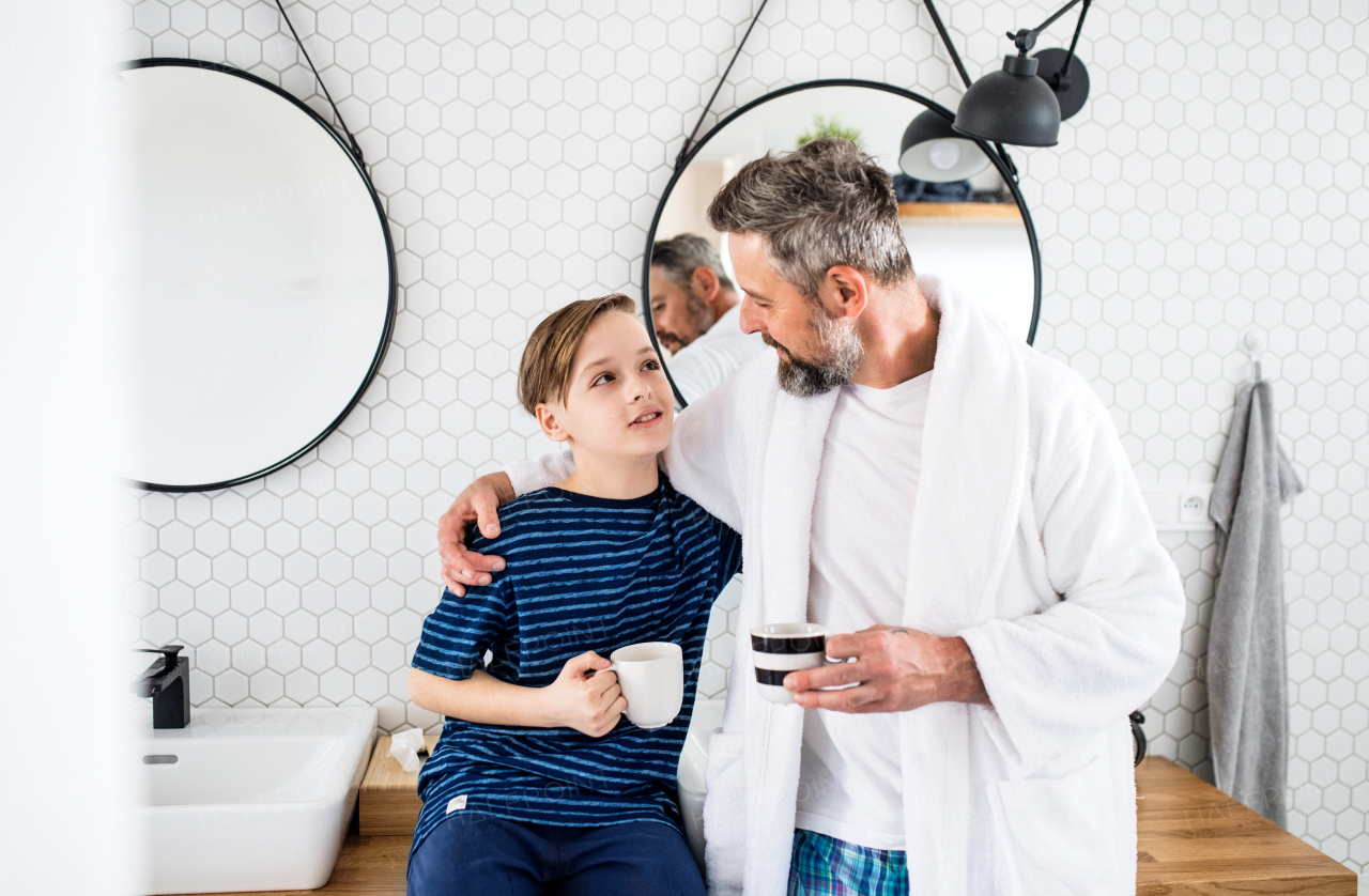 A mature father with small in the bathroom in the morning, holding cups.