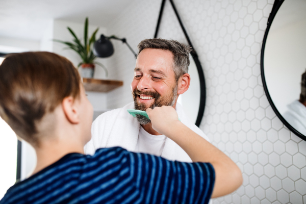 A mature father with small son in the bathroom in the morning, combing hair.