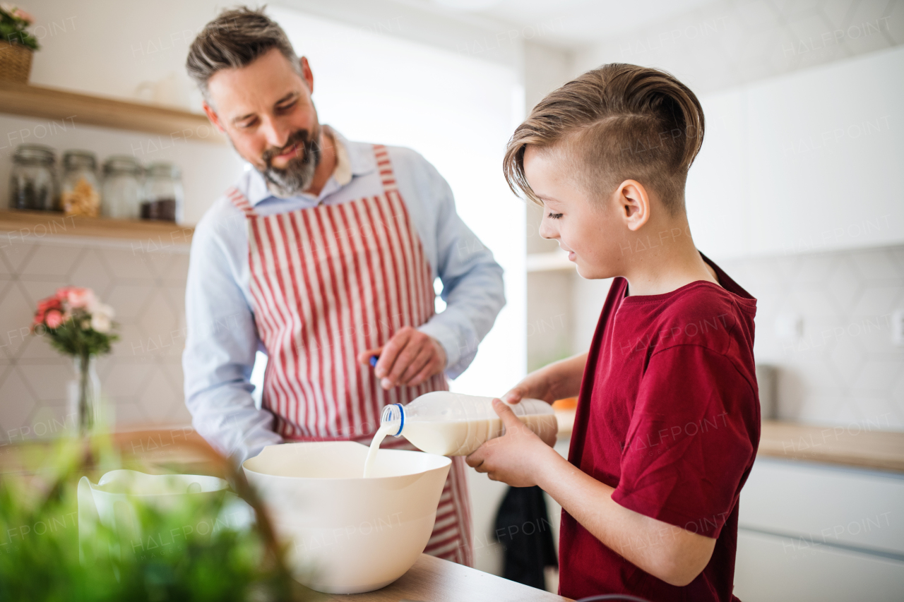 A mature father with small son indoors in kitchen, making pancakes.