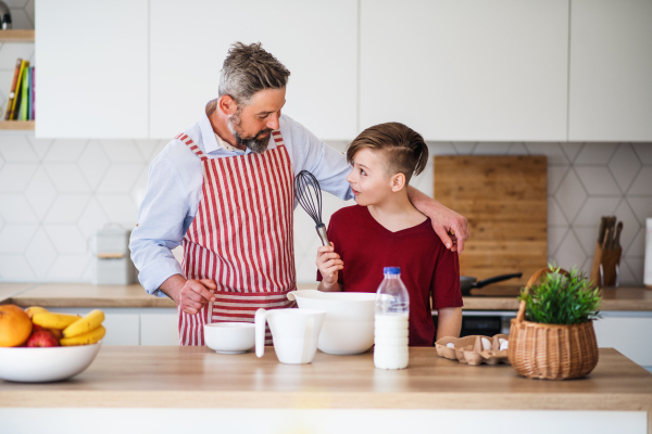 A mature father with small son indoors in kitchen, making pancakes.