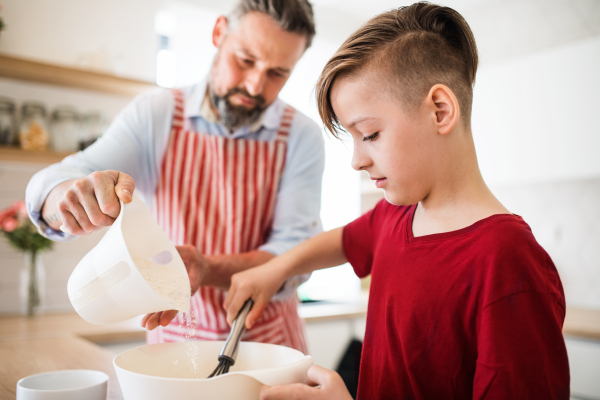 A mature father with small son indoors in kitchen, making pancakes.