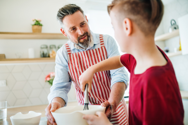 A mature father with small son indoors in kitchen, making pancakes.