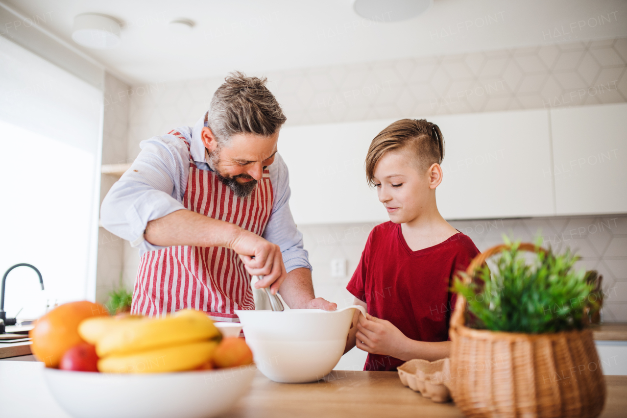 A mature father with small son indoors in kitchen, making pancakes.