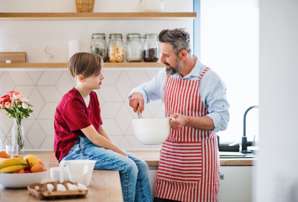 A mature father with small son indoors in kitchen, making pancakes.