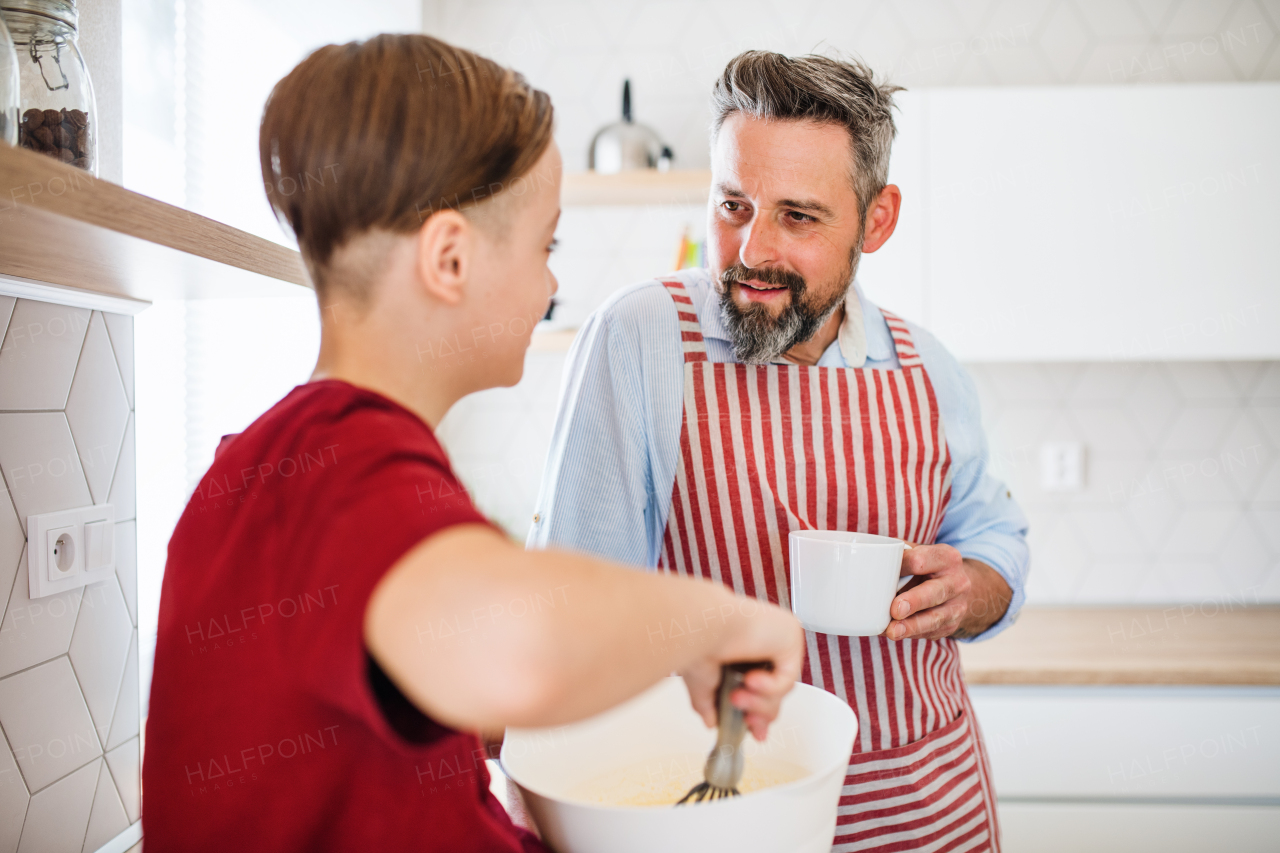 A mature father with small son indoors in kitchen, making pancakes.