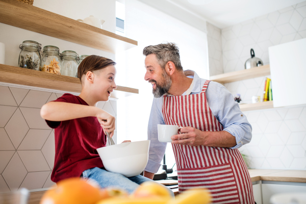 A mature father with small son indoors in kitchen, making pancakes.