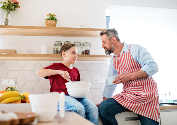 A mature father with small son indoors in kitchen, making pancakes.