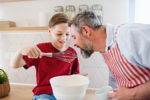 A mature father with small son indoors in kitchen, making pancakes.