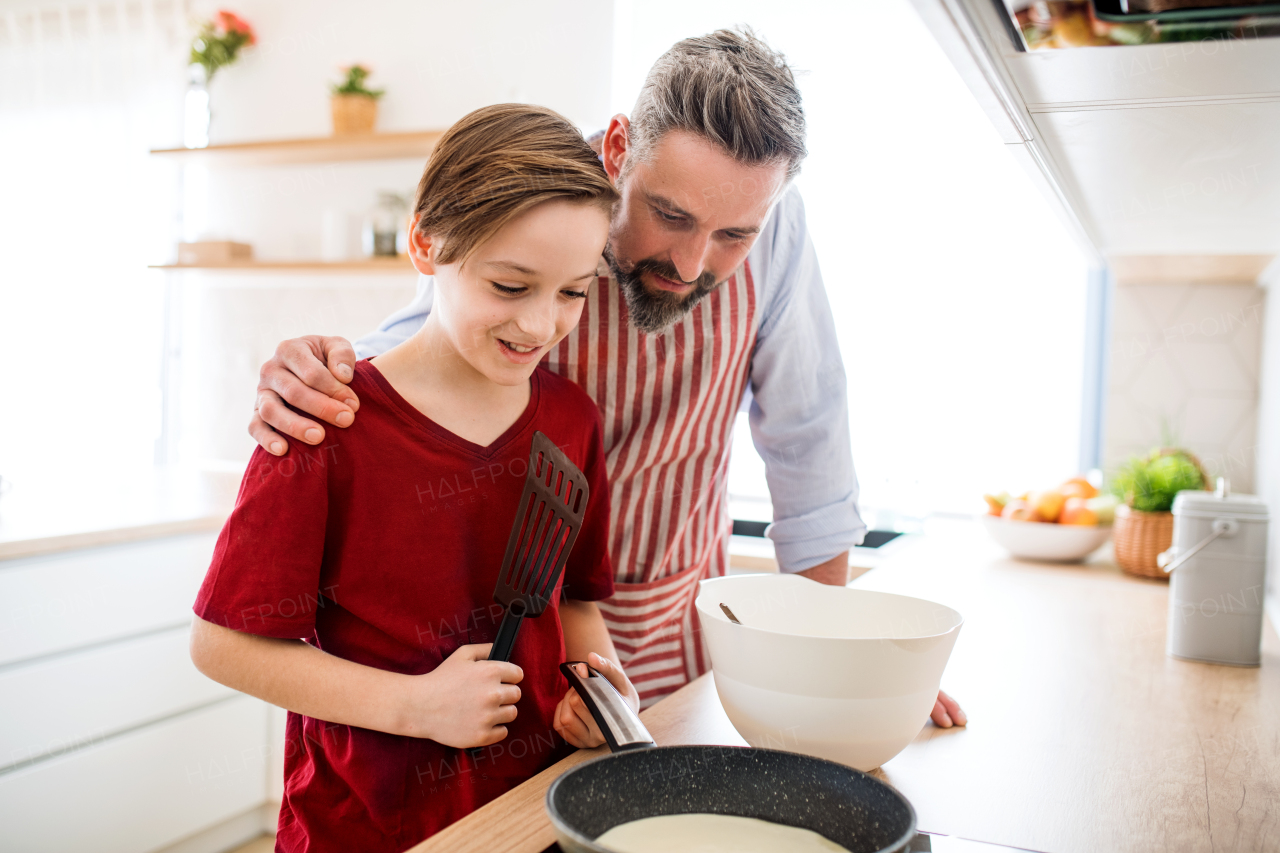 A mature father with small son indoors in kitchen, making pancakes.