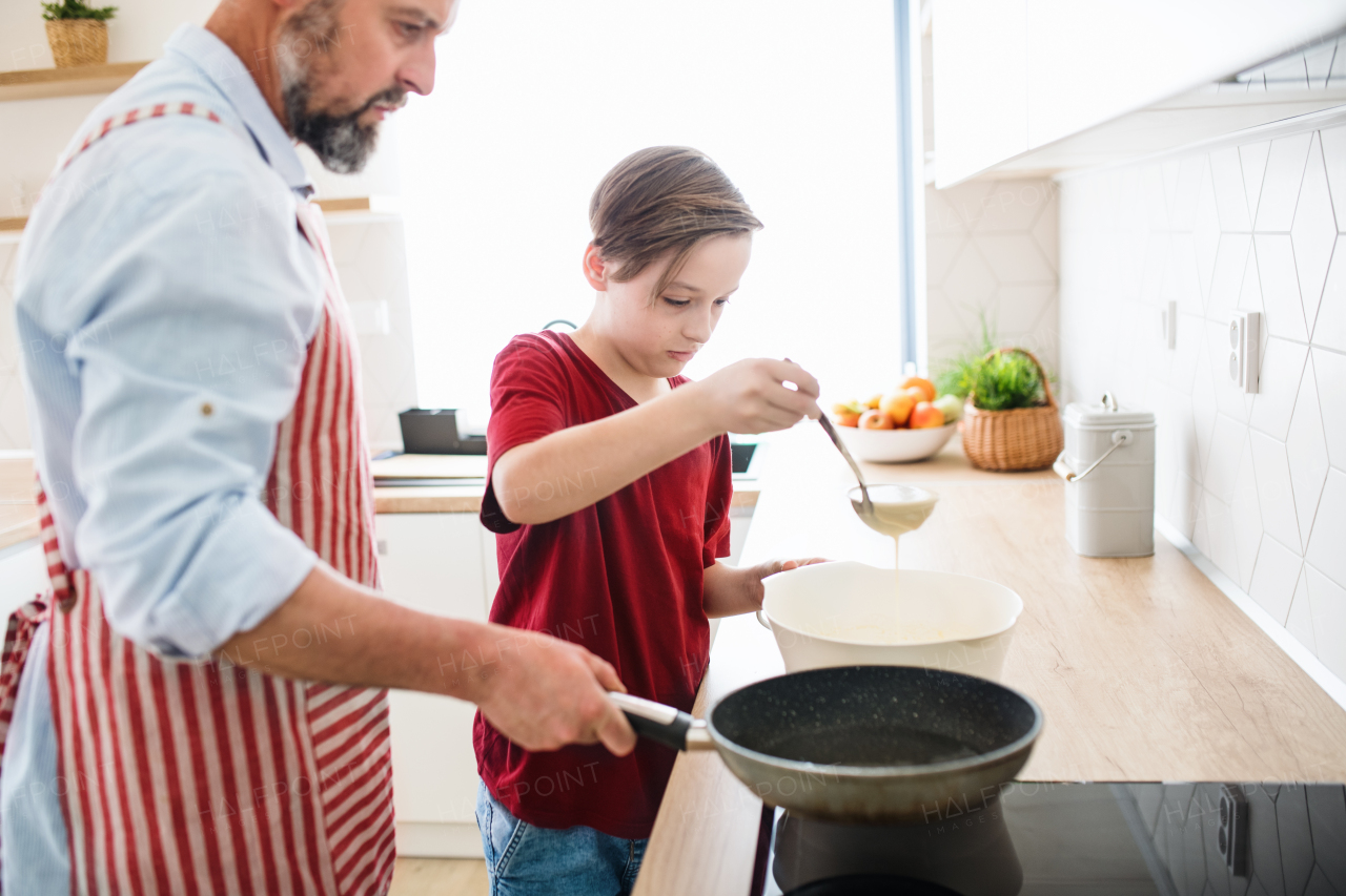 A mature father with small son indoors in kitchen, making pancakes.