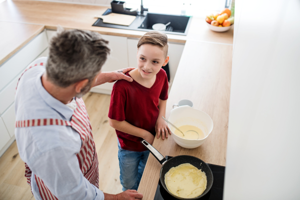 A top view of mature father with small son indoors in kitchen, making pancakes.