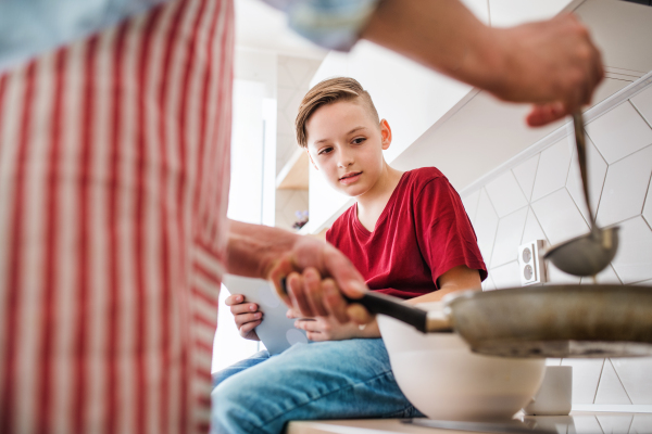 A mature father with small son indoors in kitchen, making pancakes.