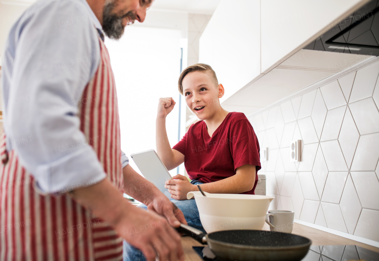 A mature father with small son indoors in kitchen, making pancakes.