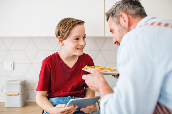 A mature father with small son indoors in kitchen, making pancakes.