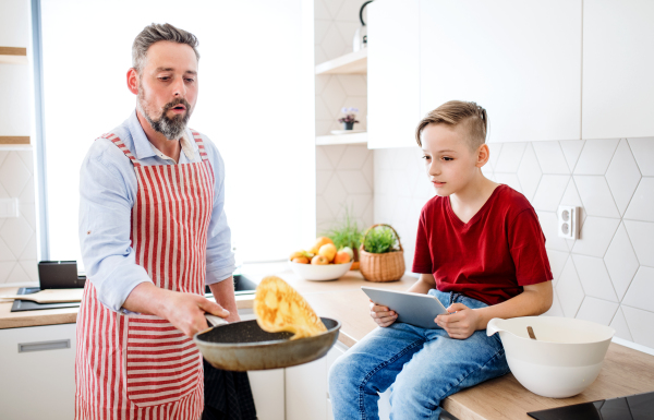 A mature father with small son indoors in kitchen, making pancakes.