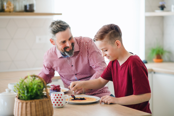 A mature father with small son indoors sitting at the table, making pancakes.