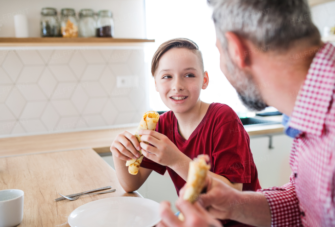 A mature father with small son indoors sitting at the table, eating pancakes.