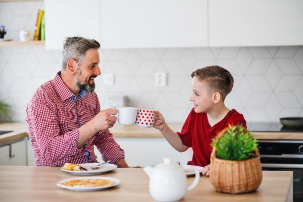 A mature father with small son indoors sitting at the table, eating pancakes.