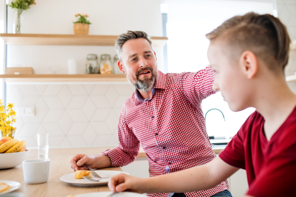 A mature father with small son indoors sitting at the table, eating pancakes.