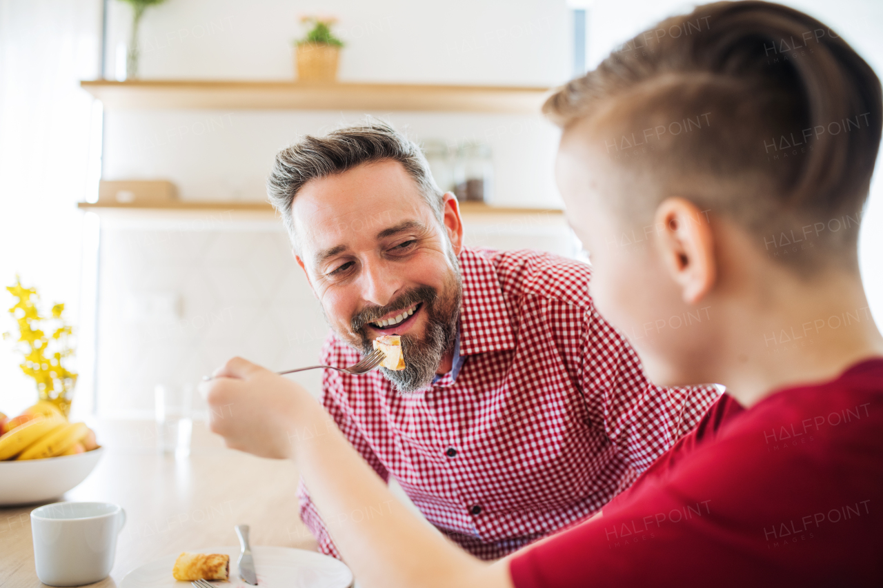 A mature father with small son indoors sitting at the table, eating pancakes.