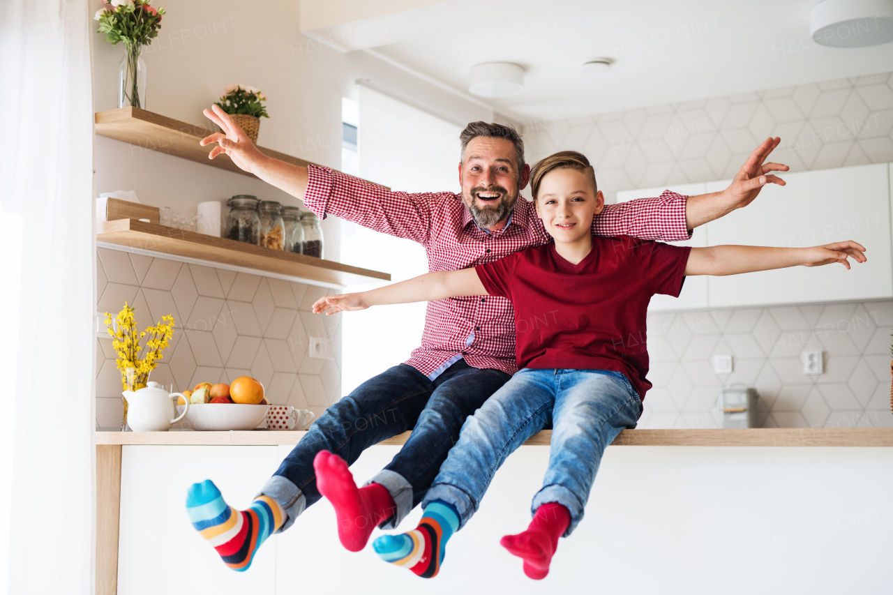 A mature father with small son sitting on kitchen counter indoors, having fun.