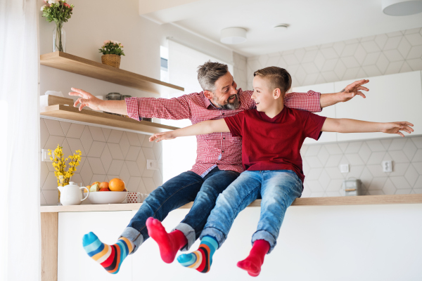 A mature father with small son sitting on kitchen counter indoors, having fun.