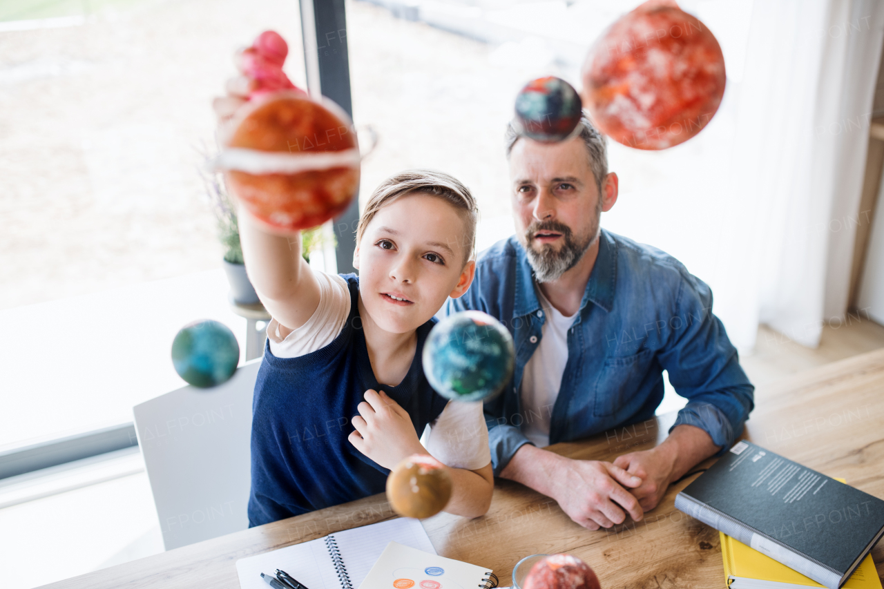 A mature father with small son sitting at table indoors, working on school project.