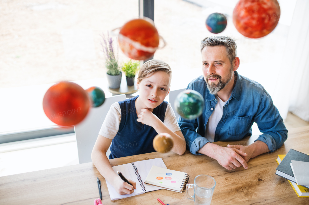 A mature father with small son sitting at table indoors, working on school project.