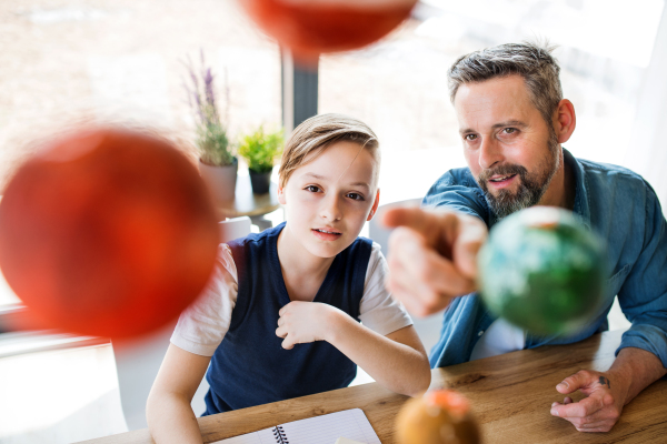 A mature father with small son sitting at table indoors, working on school project.