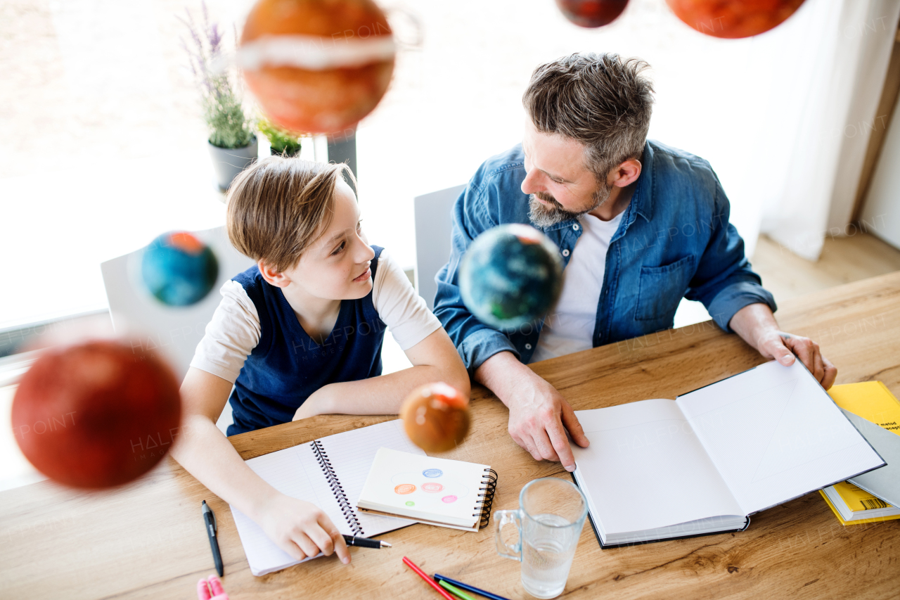 A mature father with small son sitting at table indoors, working on school project.