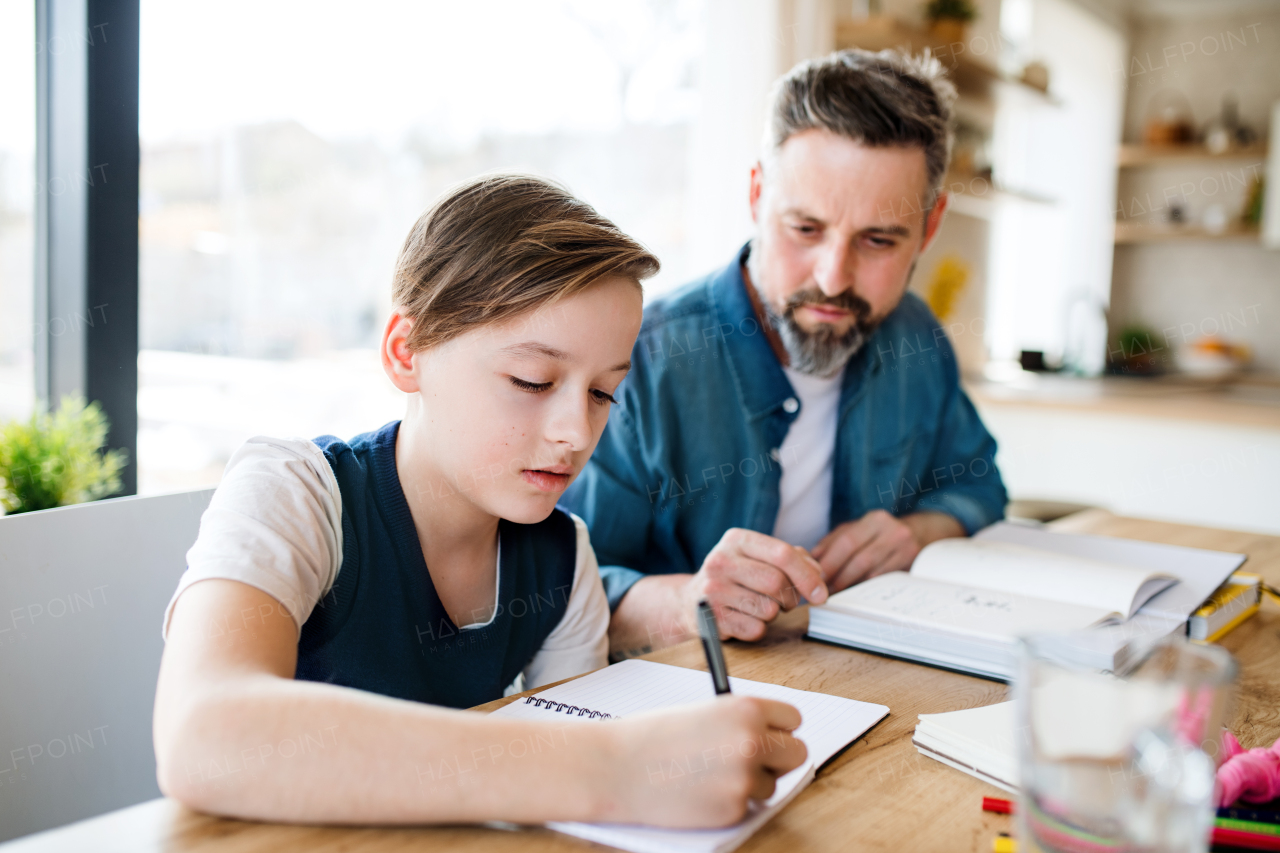 A mature father with small son sitting at table indoors, making homework.