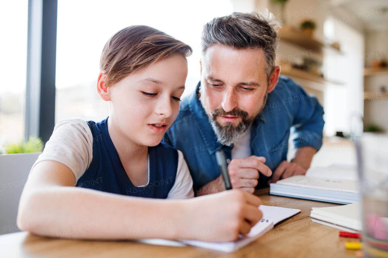 A mature father with small son sitting at table indoors, doing homework.