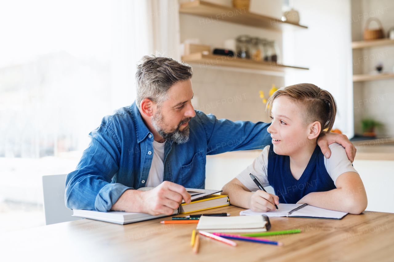 A mature father with small son sitting at table indoors, making homework.