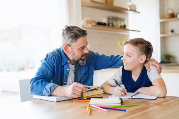 A mature father with small son sitting at table indoors, making homework.