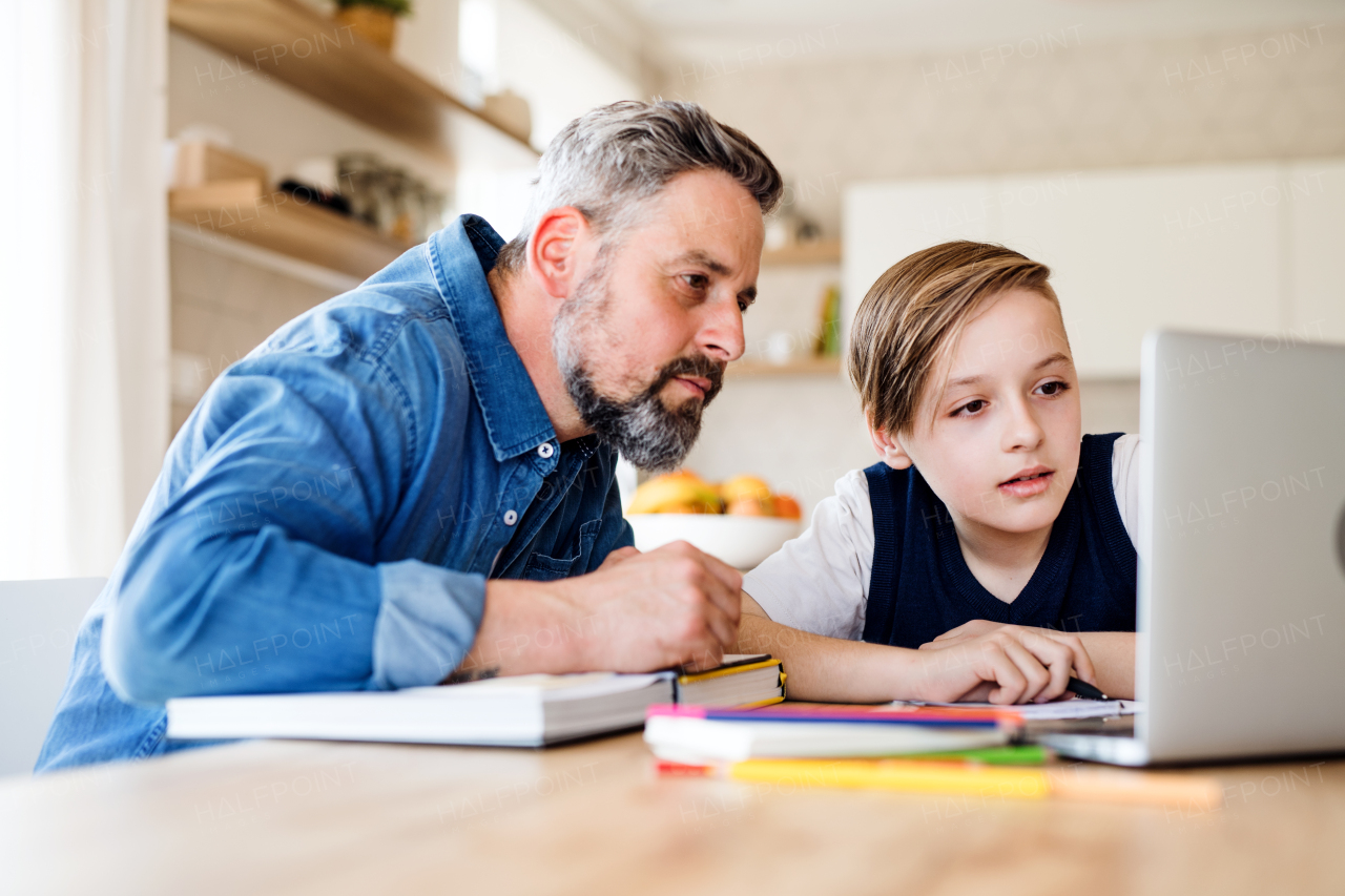 A mature father with small son sitting at table indoors, using laptop.