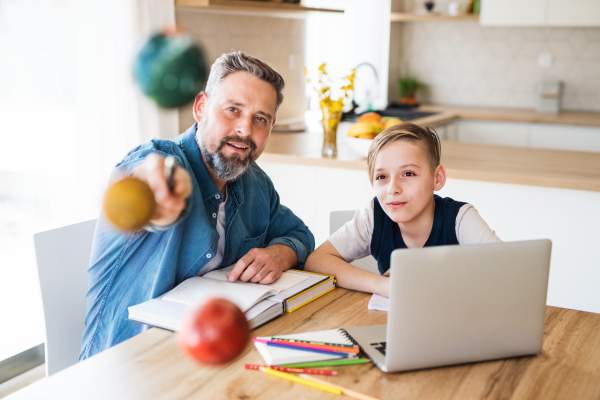 A mature father with small son sitting at table indoors, working on school project.