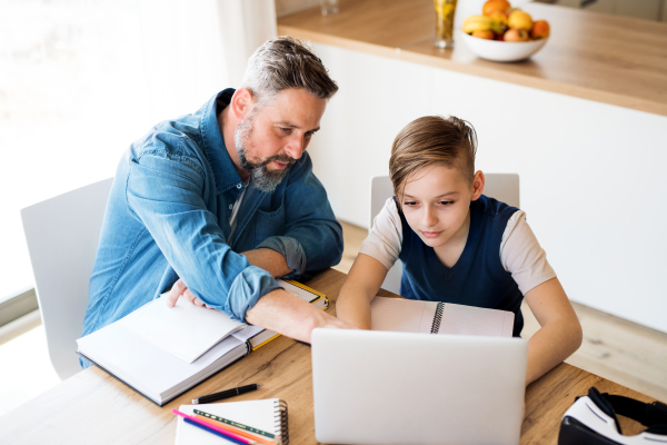 A mature father with small son sitting at table indoors, using laptop.