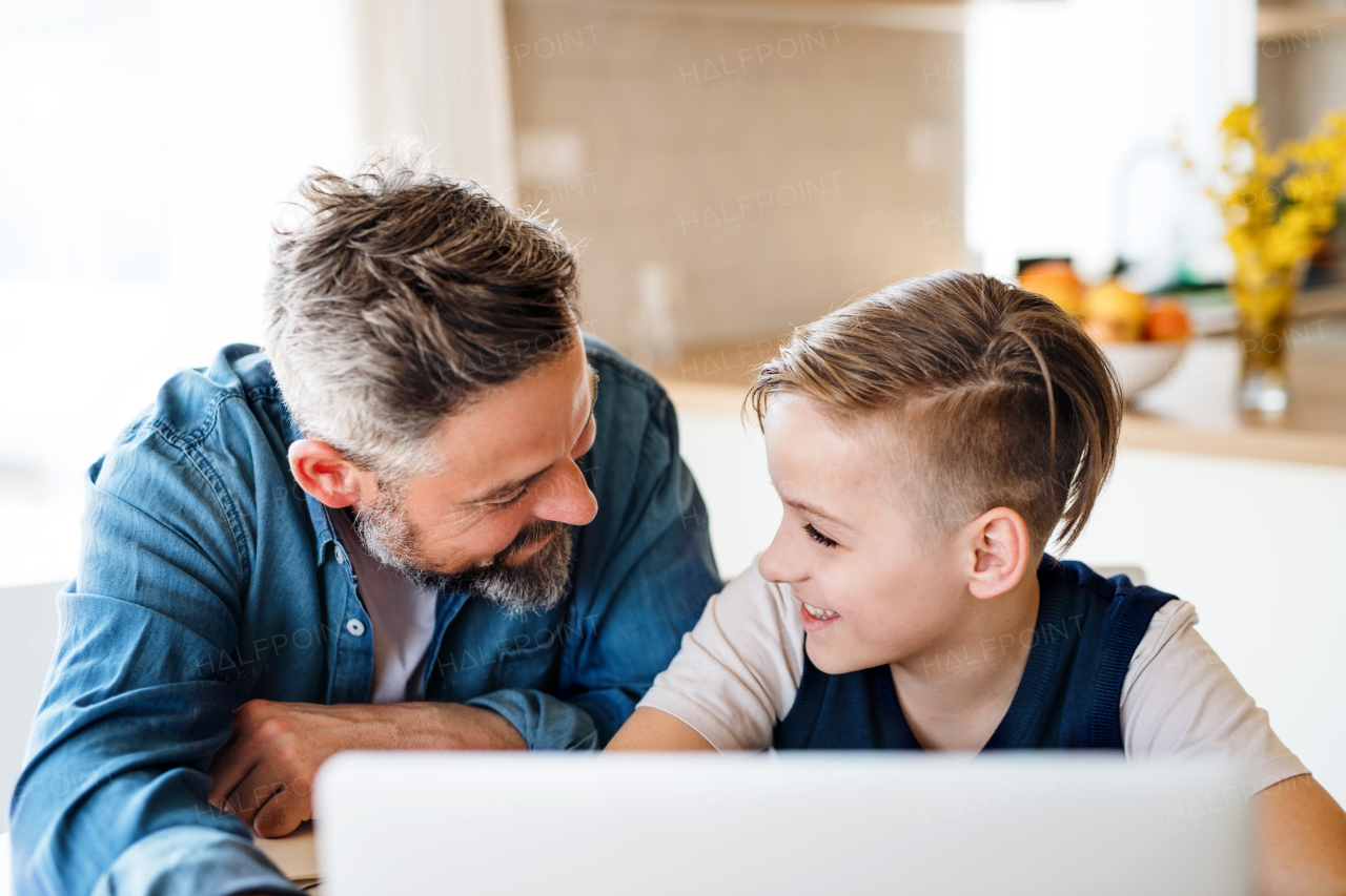 A mature father with small son sitting at table indoors, using laptop.