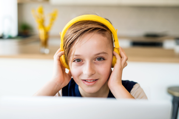 A small boy with headphones and laptop sitting at the table indoors at home.