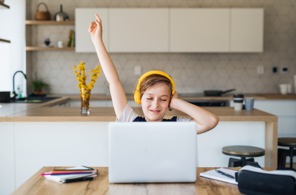 A small boy with headphones and laptop sitting at the table indoors at home.