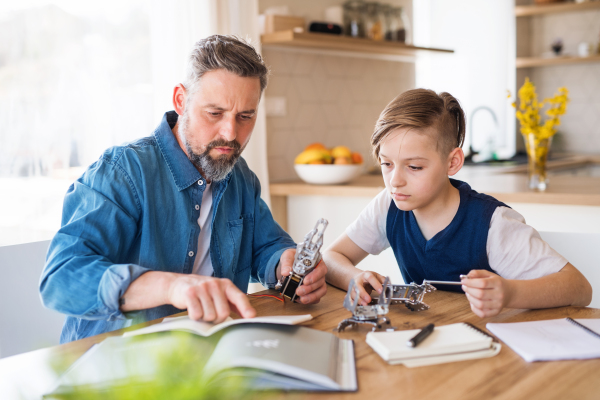 A mature father with small son sitting at table indoors, working on school project.