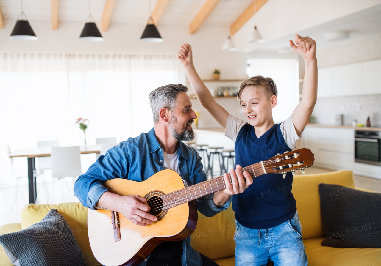 A mature father with small son sitting on sofa indoors, playing guitar.