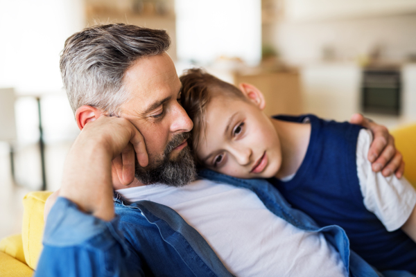 A mature father with small son sitting on sofa indoors, resting.