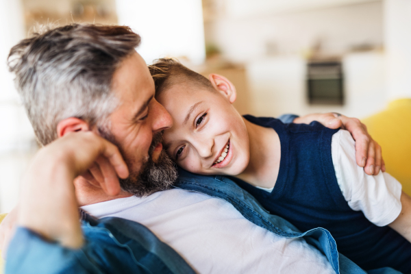 A mature father with small son sitting on sofa indoors, resting.