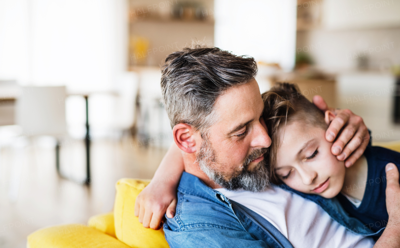 A mature father with small son sitting on sofa indoors, resting.