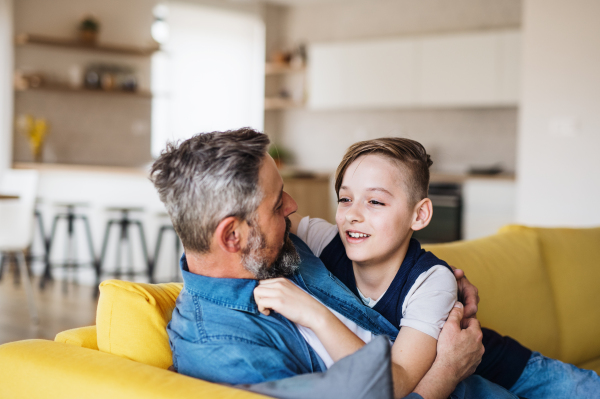 A mature father with small son sitting on sofa indoors, resting.