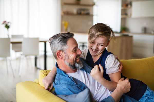 A mature father with small son sitting on sofa indoors, having fun.