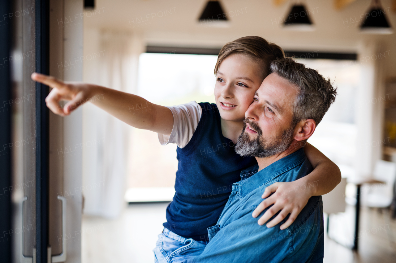 Mature father holding small son indoors, looking out of window and pointing to something.