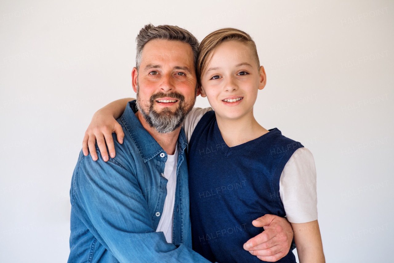 A mature father and small son standing indoors, looking at camera.