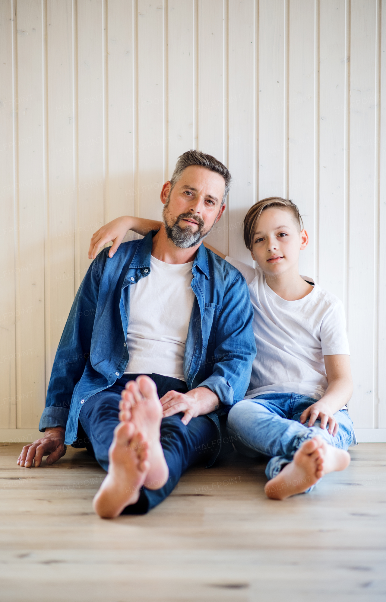 Mature father with small son sitting indoors ont the floor, looking at camera.